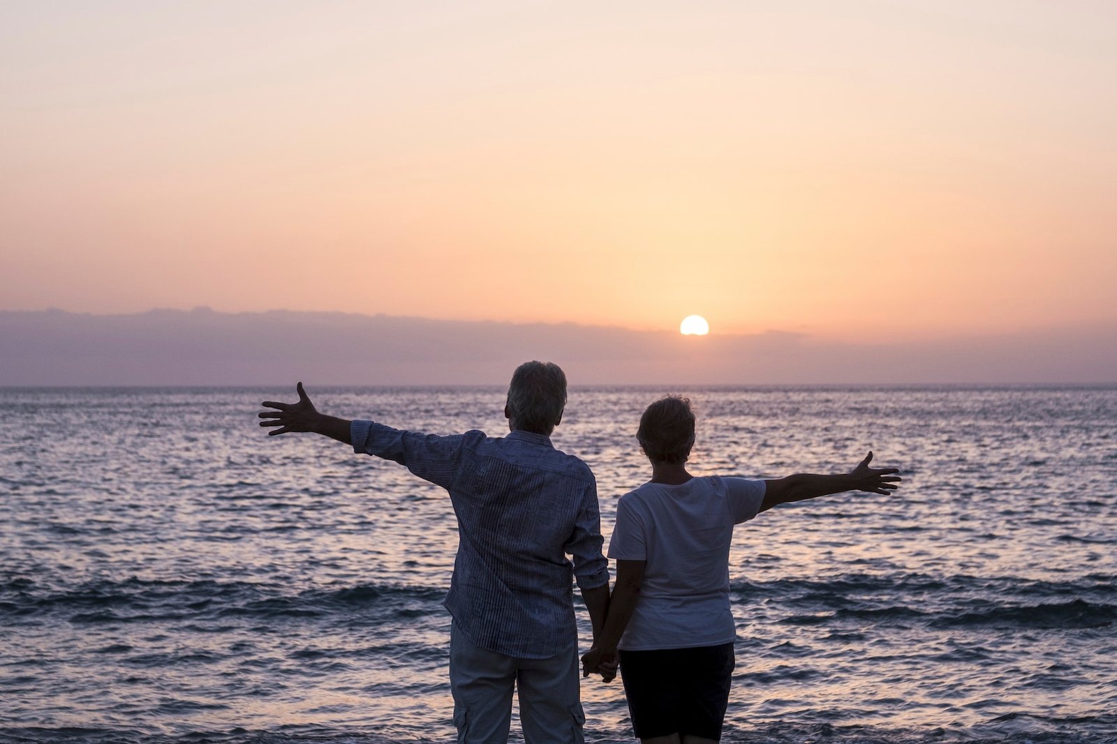 Happy senior couple people in love enjoy a sunset on the ocean holding hands - love and relationship